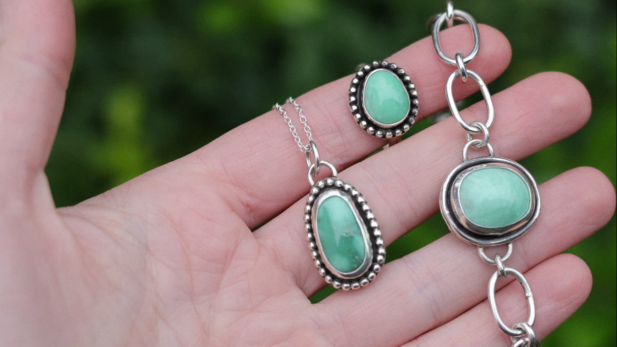 Turquoise stone jewelry set on a hand with a green blurred background