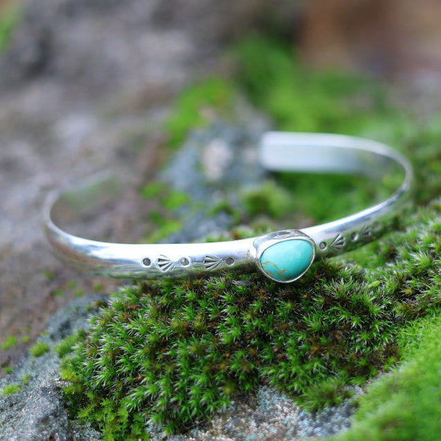 Silver cuff bracelet with a kingman turquoise stone on a mossy rock